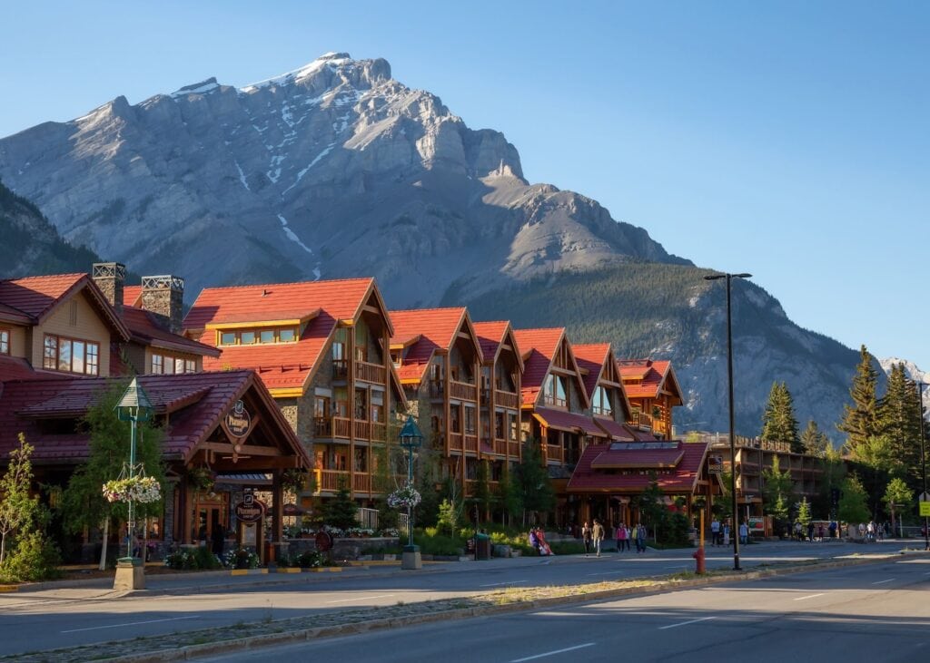 The main avenue of the town of Banff lined with alpine lodges, with a rugged mountain rising behind it in Alberta, Canada.