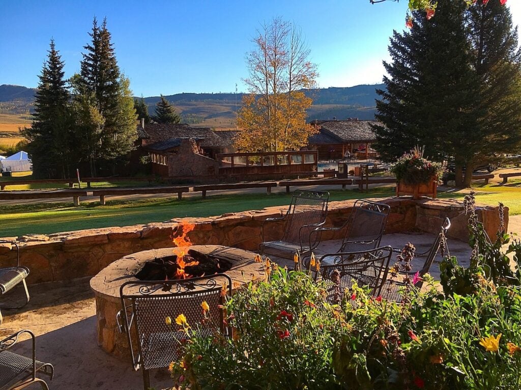 An outdoor stone fire pit with seating at C Lazy U Ranch in Colorado with rolling hills and autumn trees in the background.