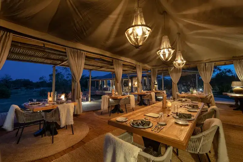 Elegant open air dining area at a luxury safari tented camp illuminated by lanterns at dusk