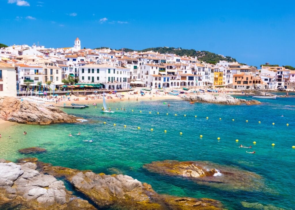 Whitewashed coastal village of Calella de Palafrugell on the Costa Brava Spain with a rocky shoreline, turquoise water, and swimmers in the bay